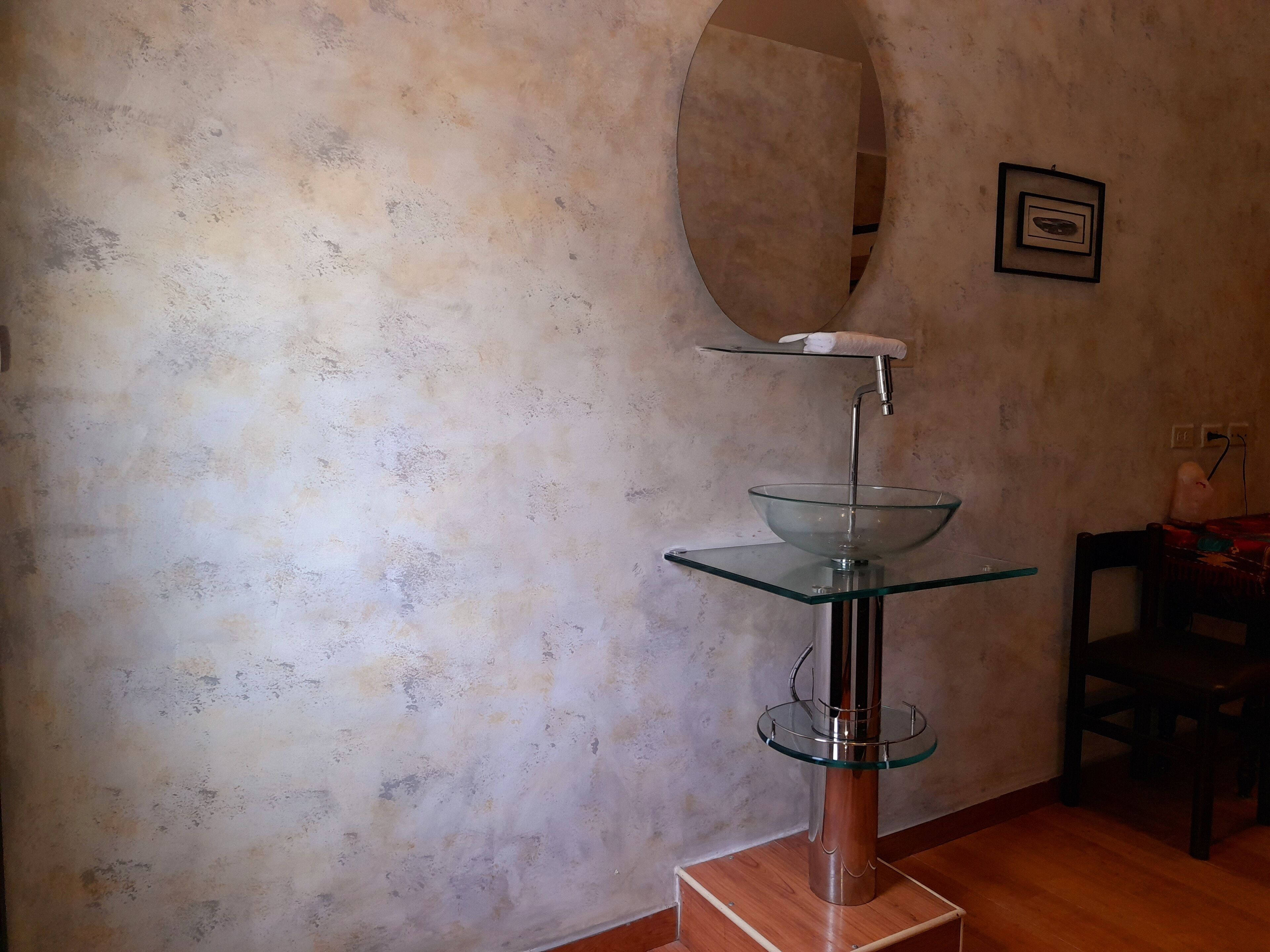 A bathroom with a glass sink on a wooden pedestal, a towel rack above it, and a mirror on the wall.