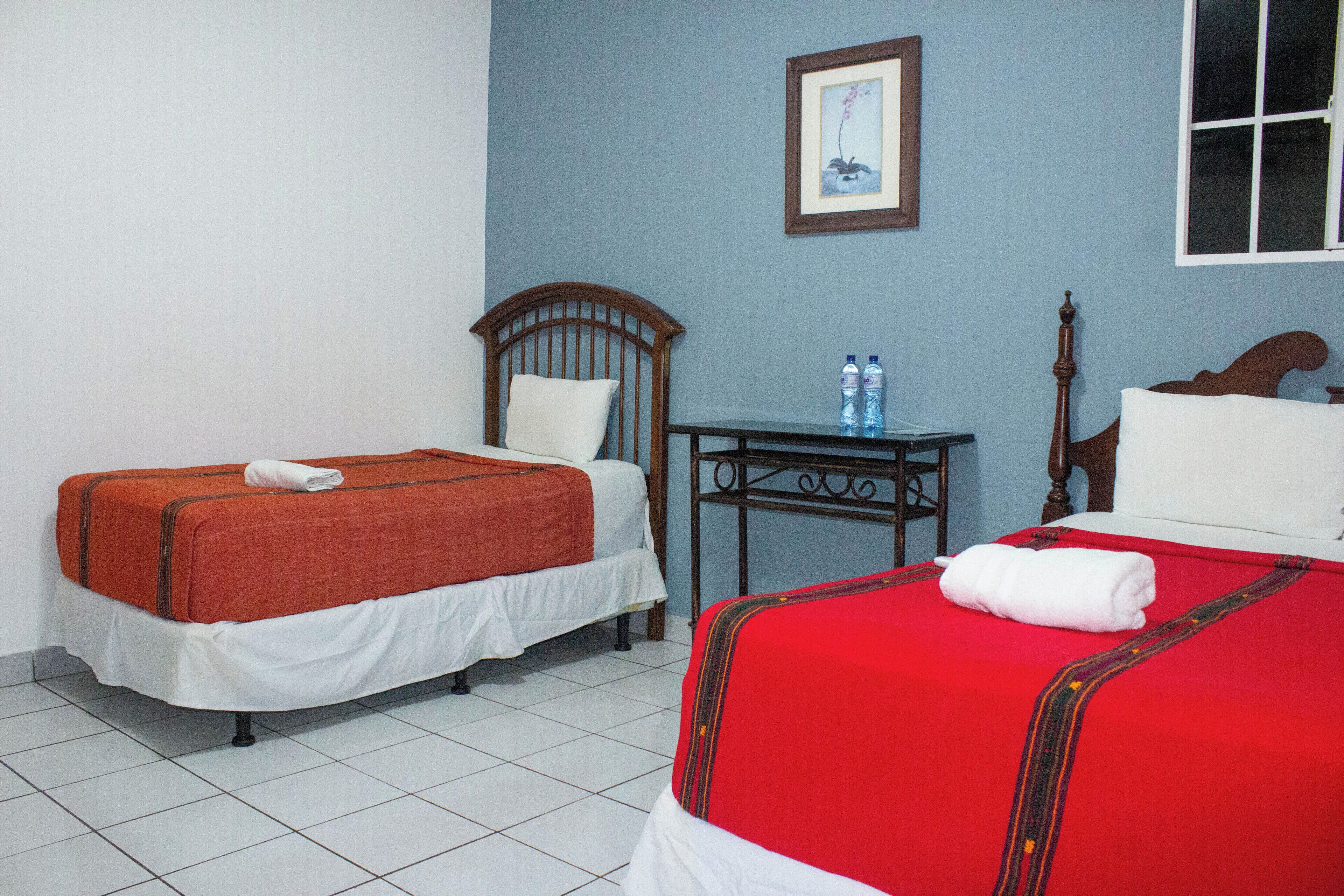 A hotel room with two single beds, a small table, and a framed picture on the wall.