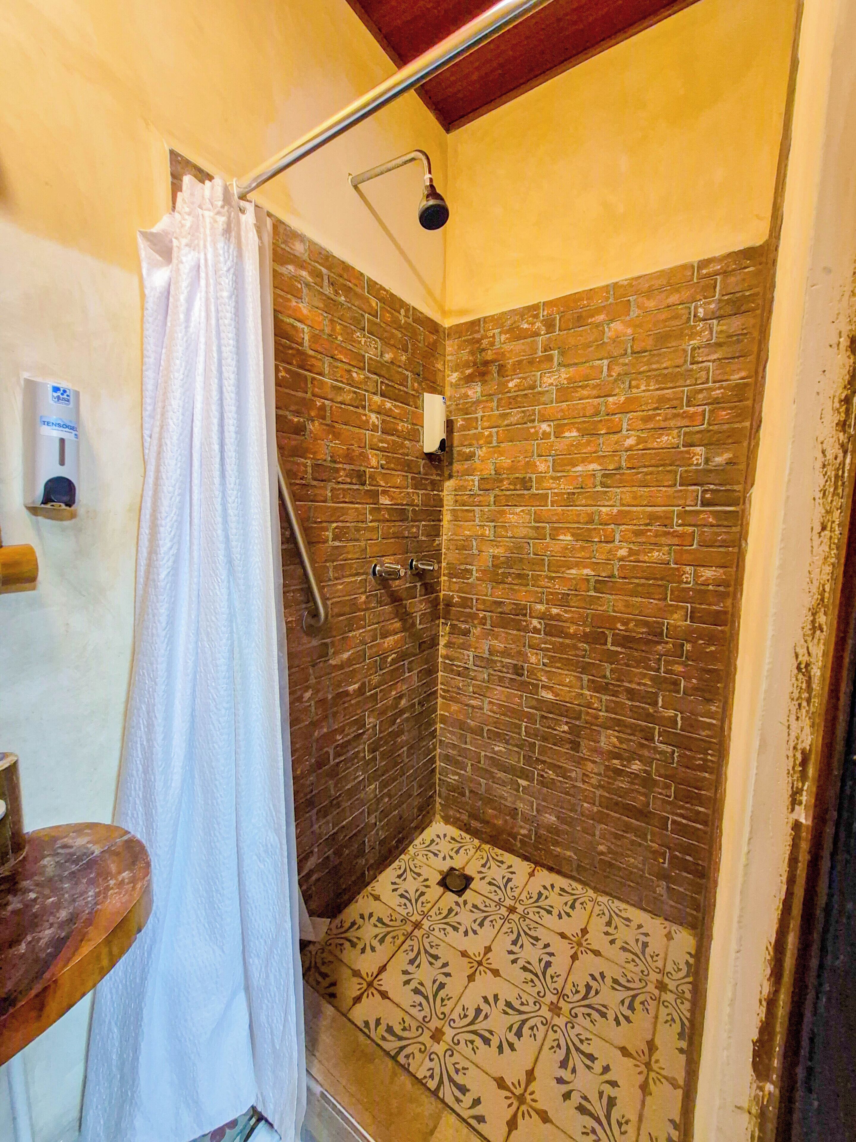Een douche met een bakstenen muur, een wit douchegordijn en een handdouche.