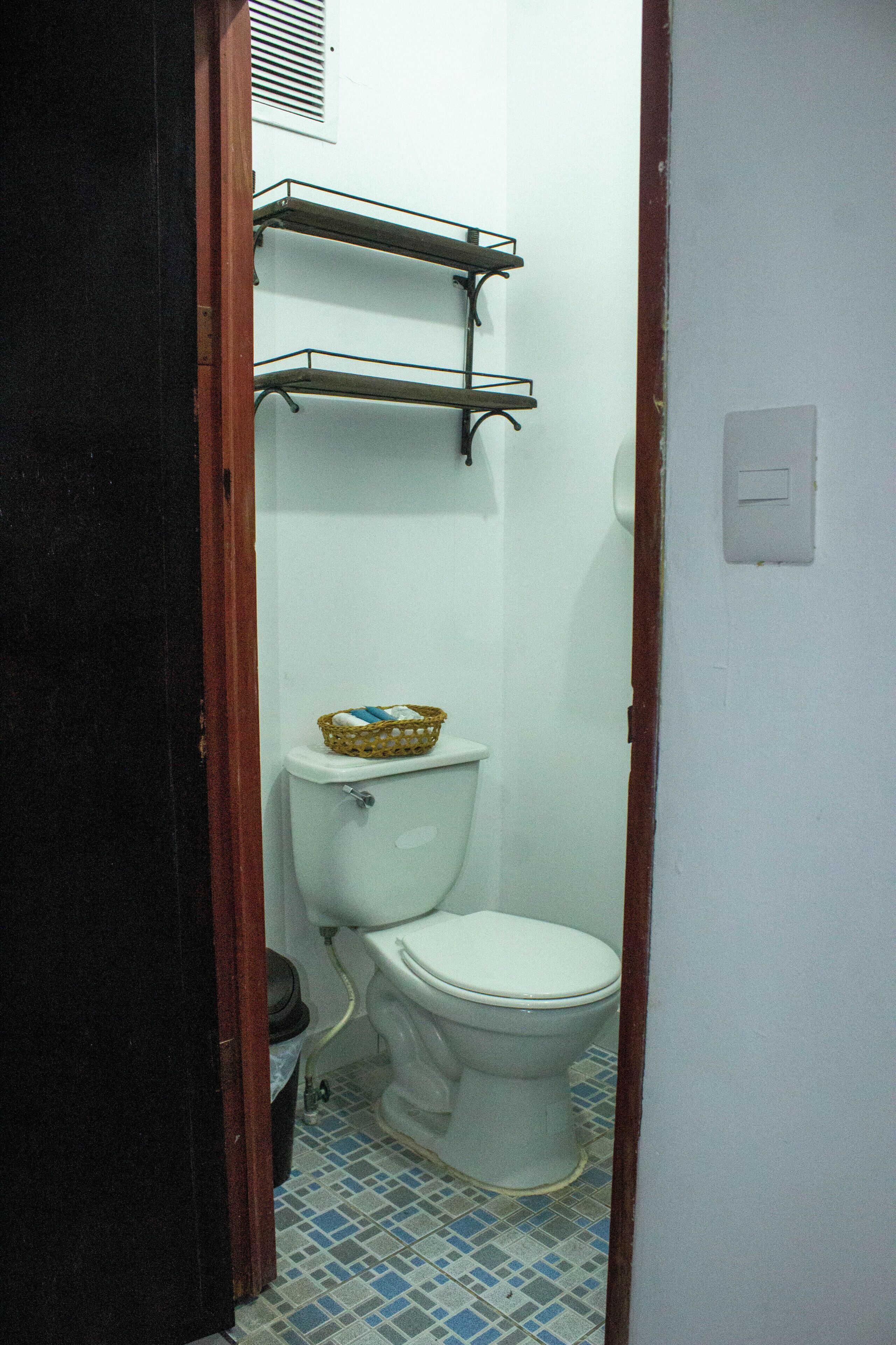 A narrow bathroom with a toilet, a basket on the tank, and a tiled floor.