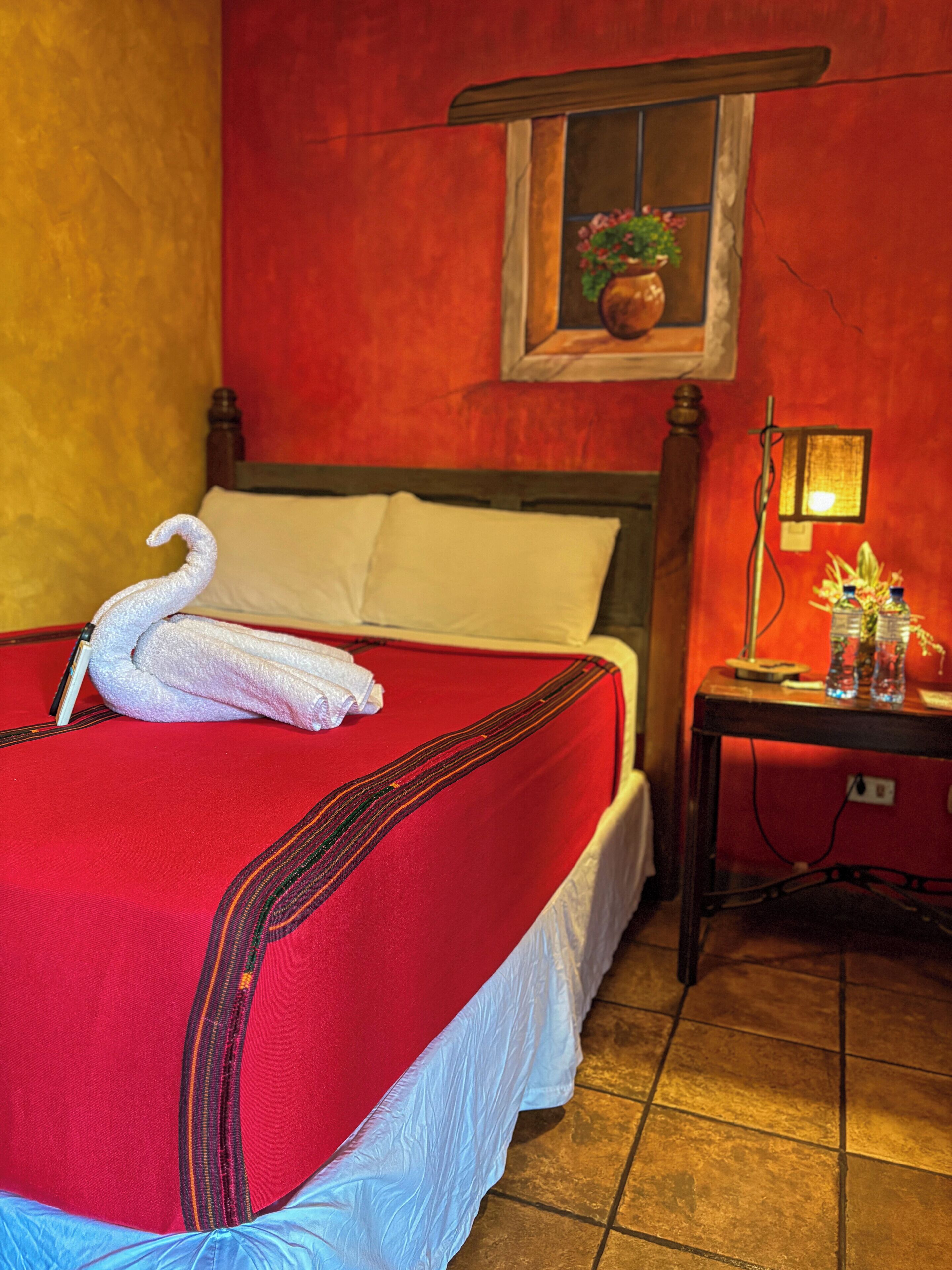 Una cama con una colcha roja, un almohadón blanco y una decoración con forma de cisne.