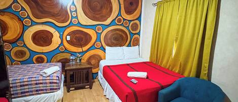 A room with two beds, a blue chair, a wooden floor, and a wall with a circular pattern.