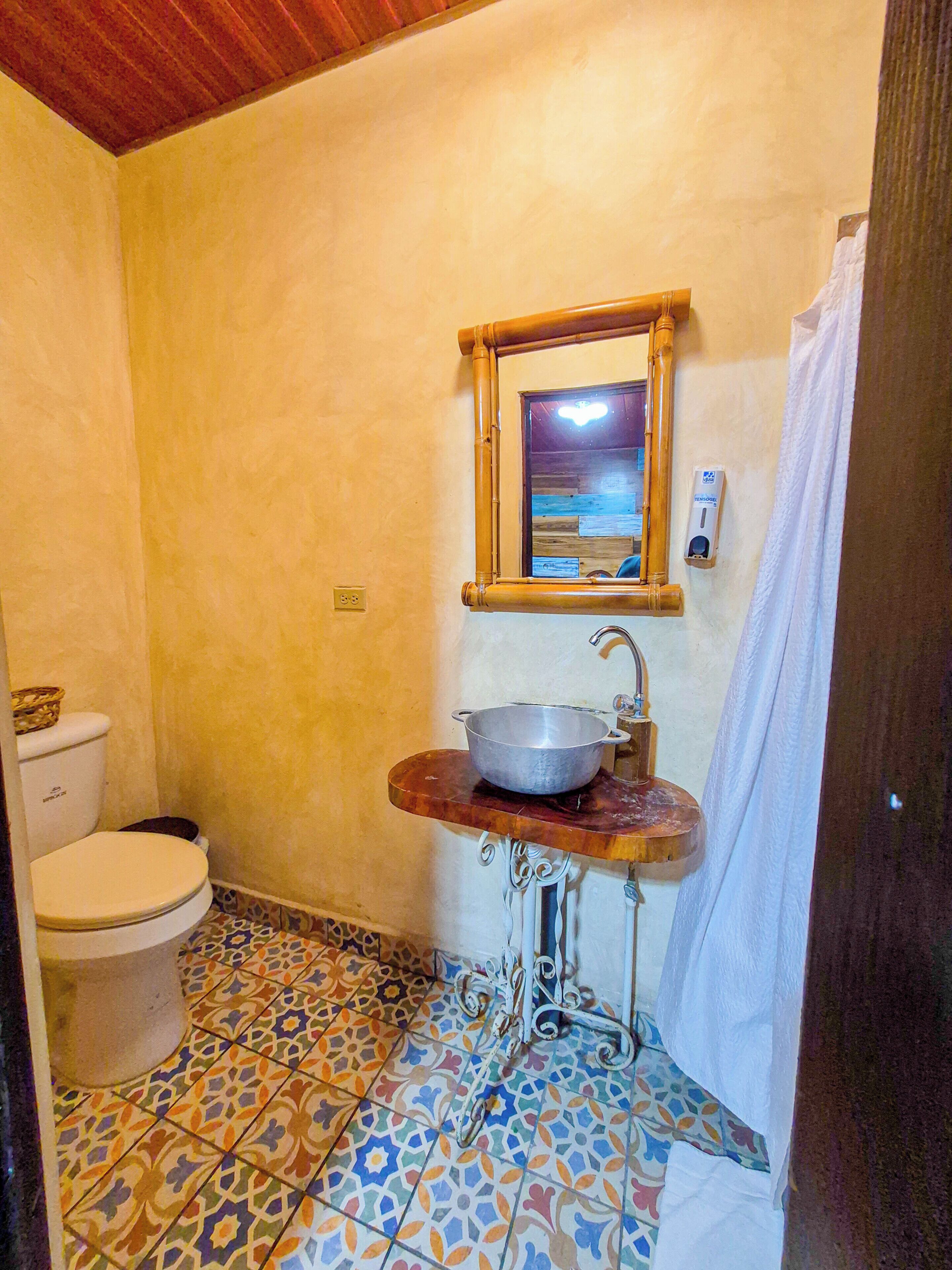Un baño con inodoro, lavabo, espejo y cortina de ducha.