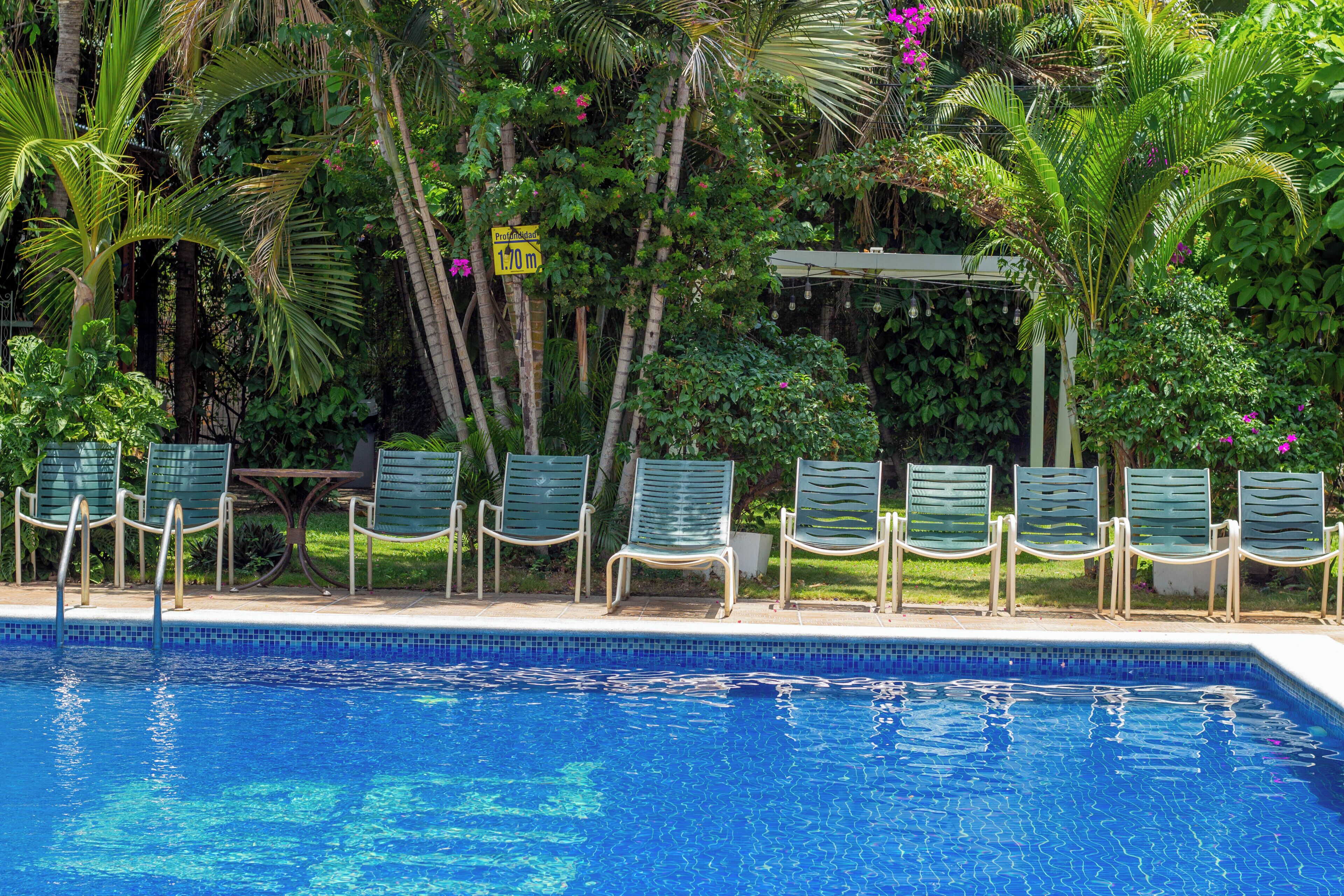 A swimming pool with lounge chairs and a pergola, surrounded by lush greenery.