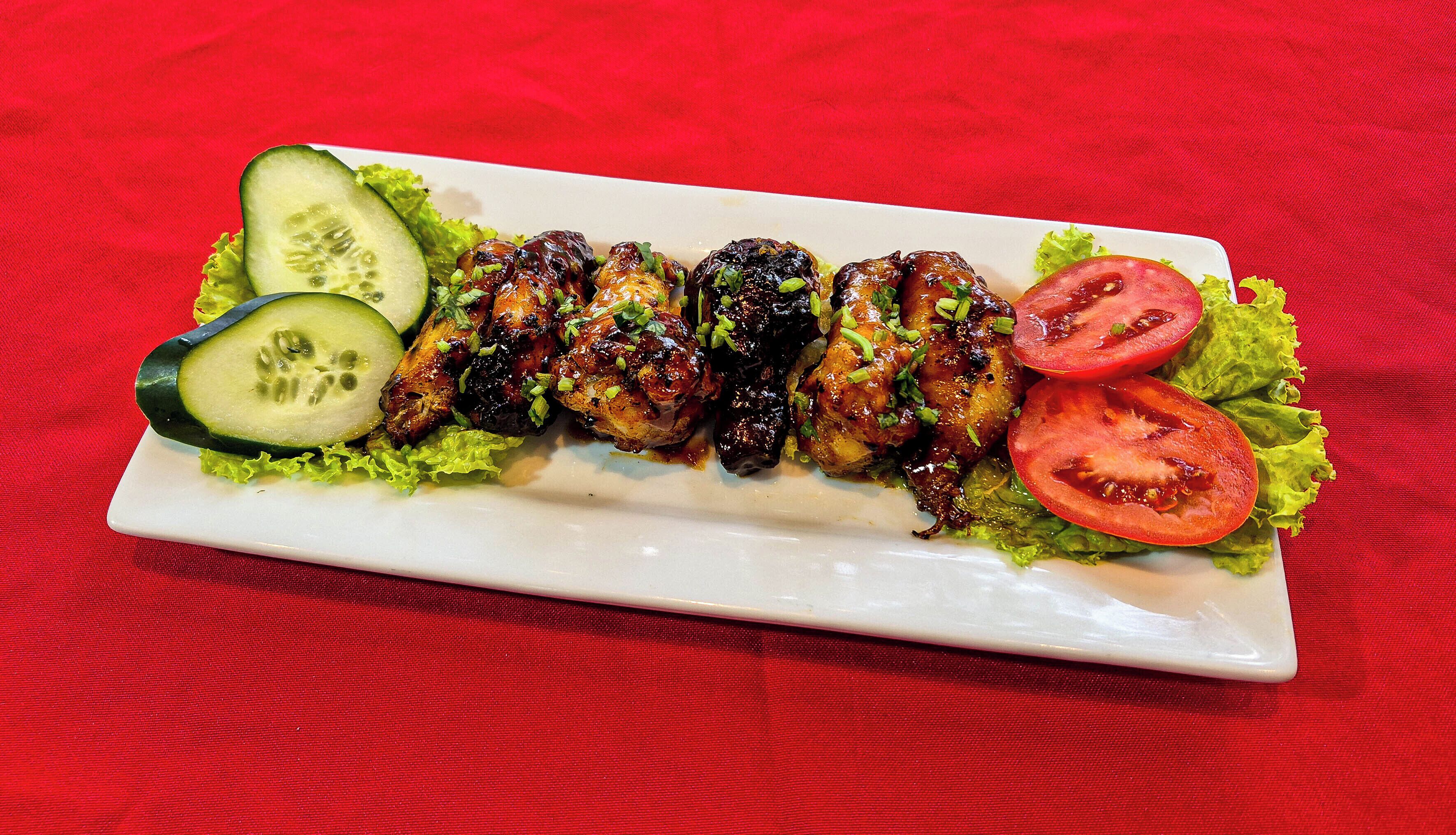 A plate of grilled chicken wings with lettuce and tomato slices.