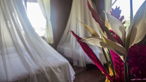 A room with a bed covered in white sheets, a window with sheer curtains, and a vase with red flowers. - Casa Grande Ecolodge at Pacuare Reserve (Matina)