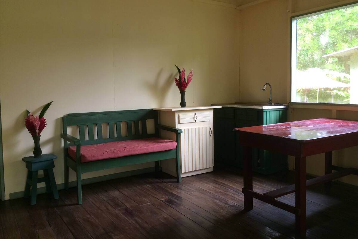 A room with a wooden bench, a small table, a cabinet, and a window with a view of greenery.