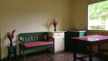 Een kamer met een houten bankje, een tafeltje, een kast en een raam met uitzicht op groen.