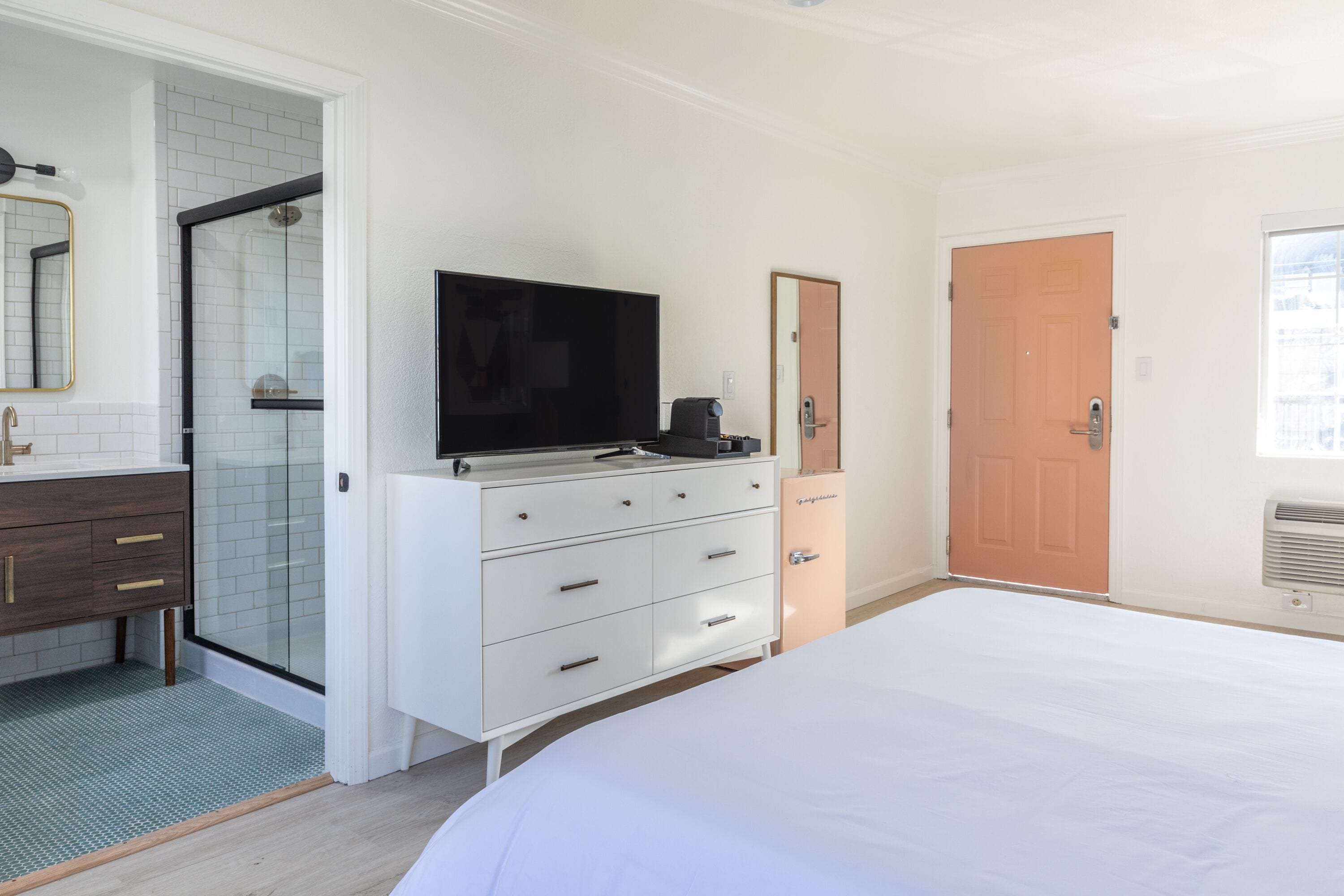 A bedroom with a bed, a TV, a dresser, a door, and a shower.