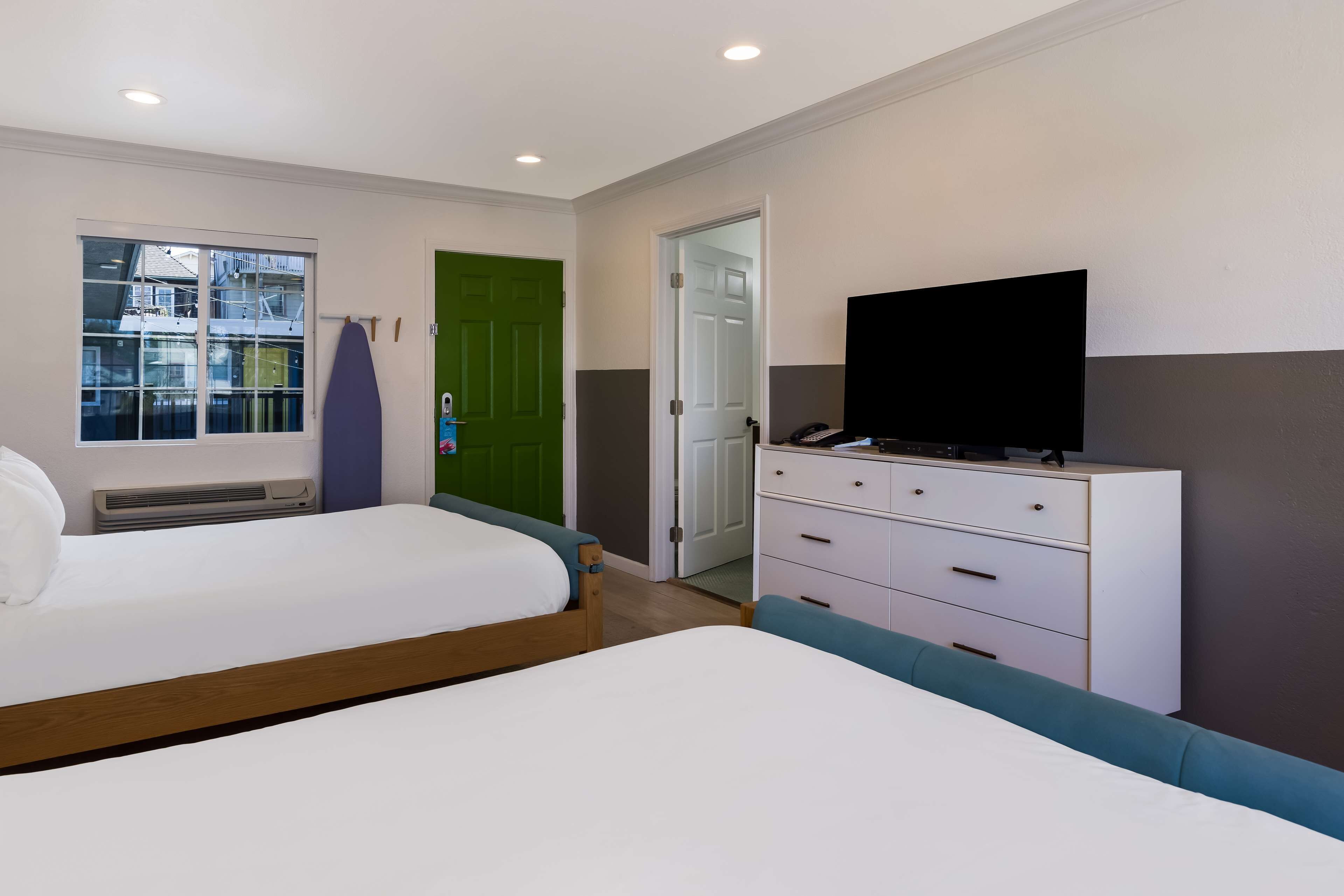 Un dormitorio con dos camas, televisor, cómoda y una puerta verde.