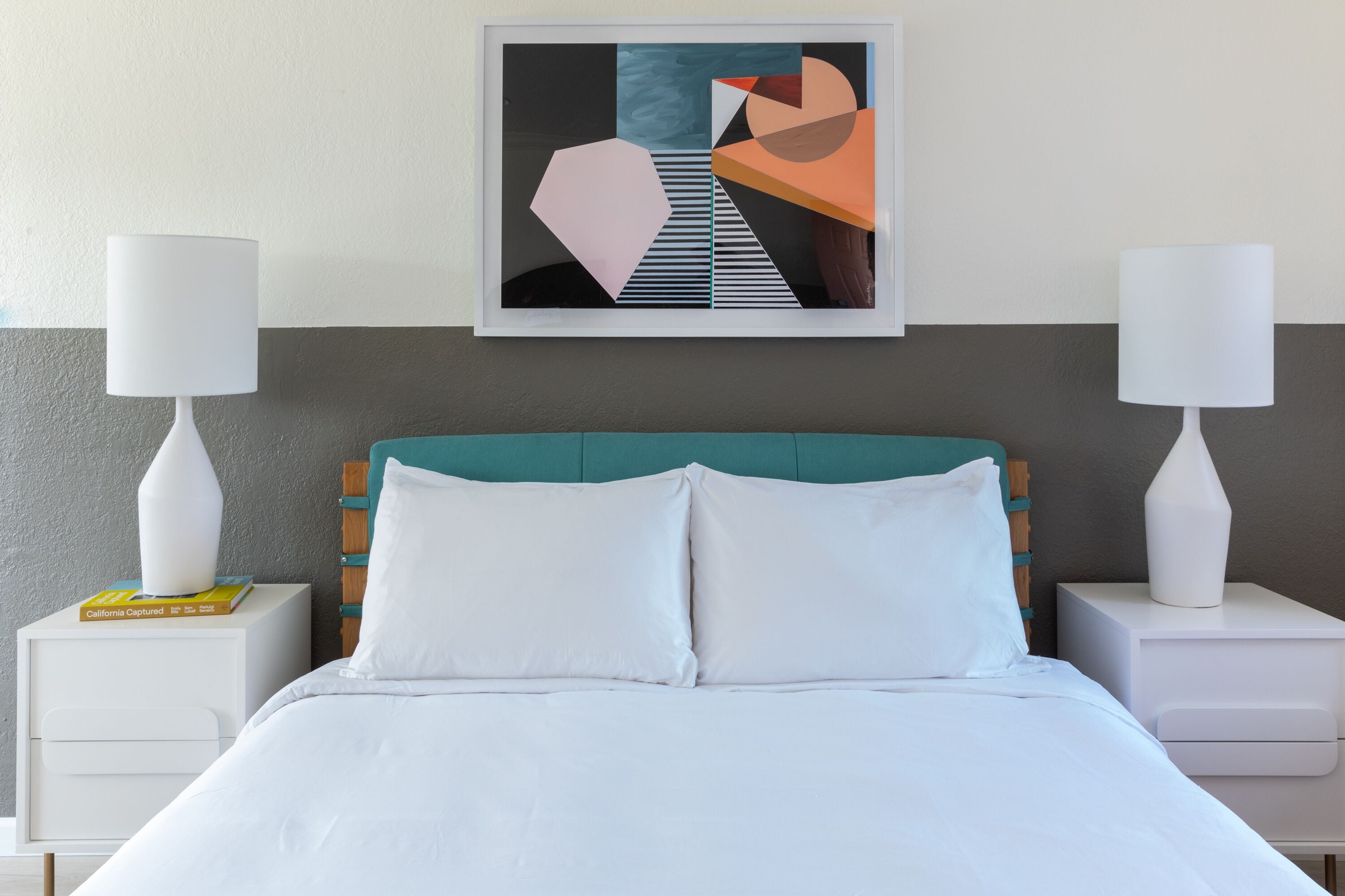 A neatly made bed with white linens, a teal headboard, and two bedside tables with white lamps.