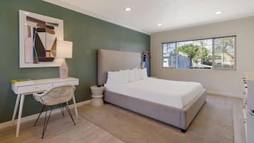 A bedroom with a bed, a desk, a chair, a lamp, and a window.