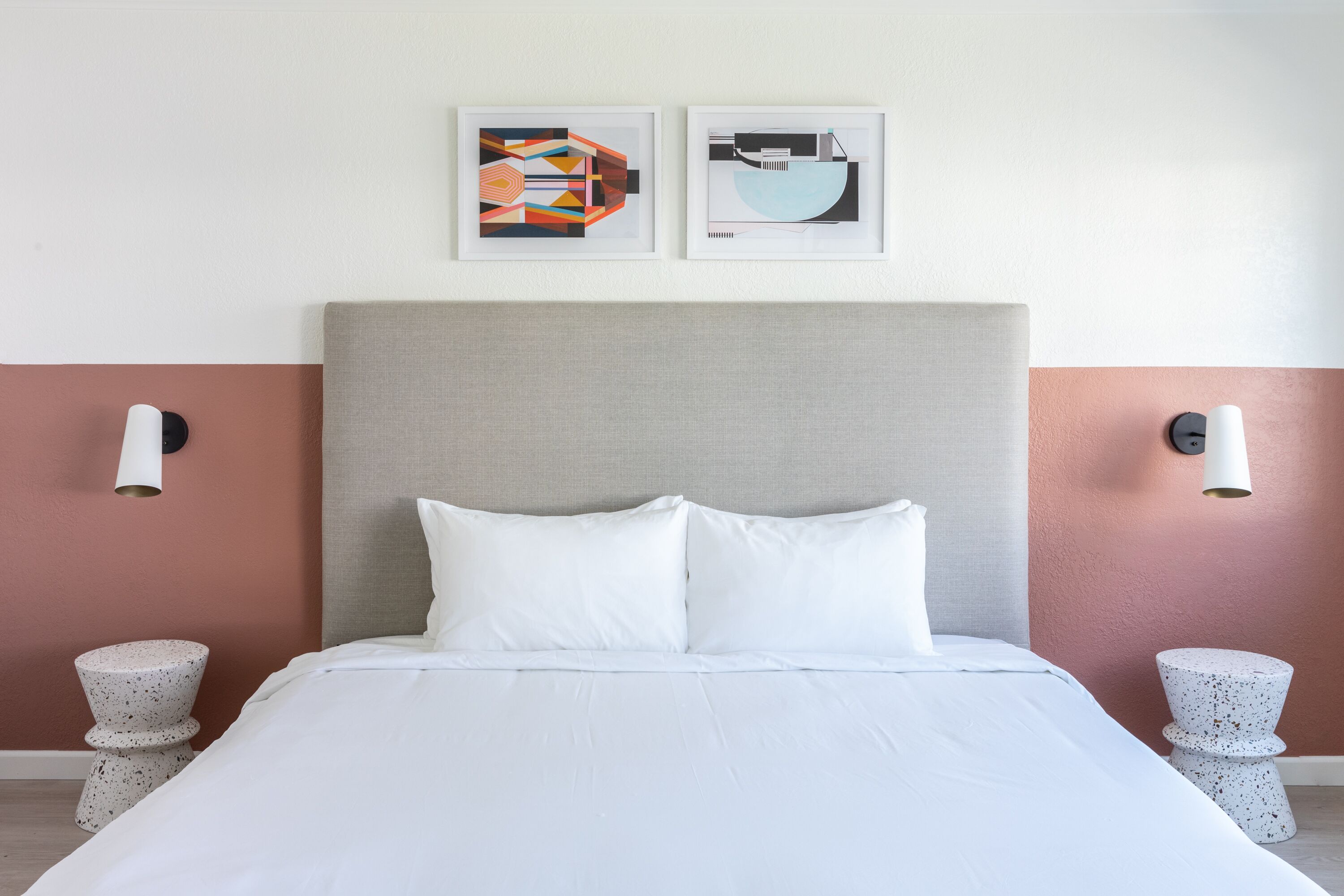 A neatly made bed with white linens, a grey upholstered headboard, and two wall-mounted light fixtures.