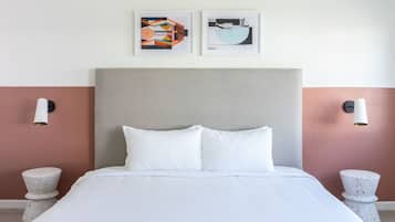 A neatly made bed with white linens, a grey upholstered headboard, and two wall-mounted light fixtures.