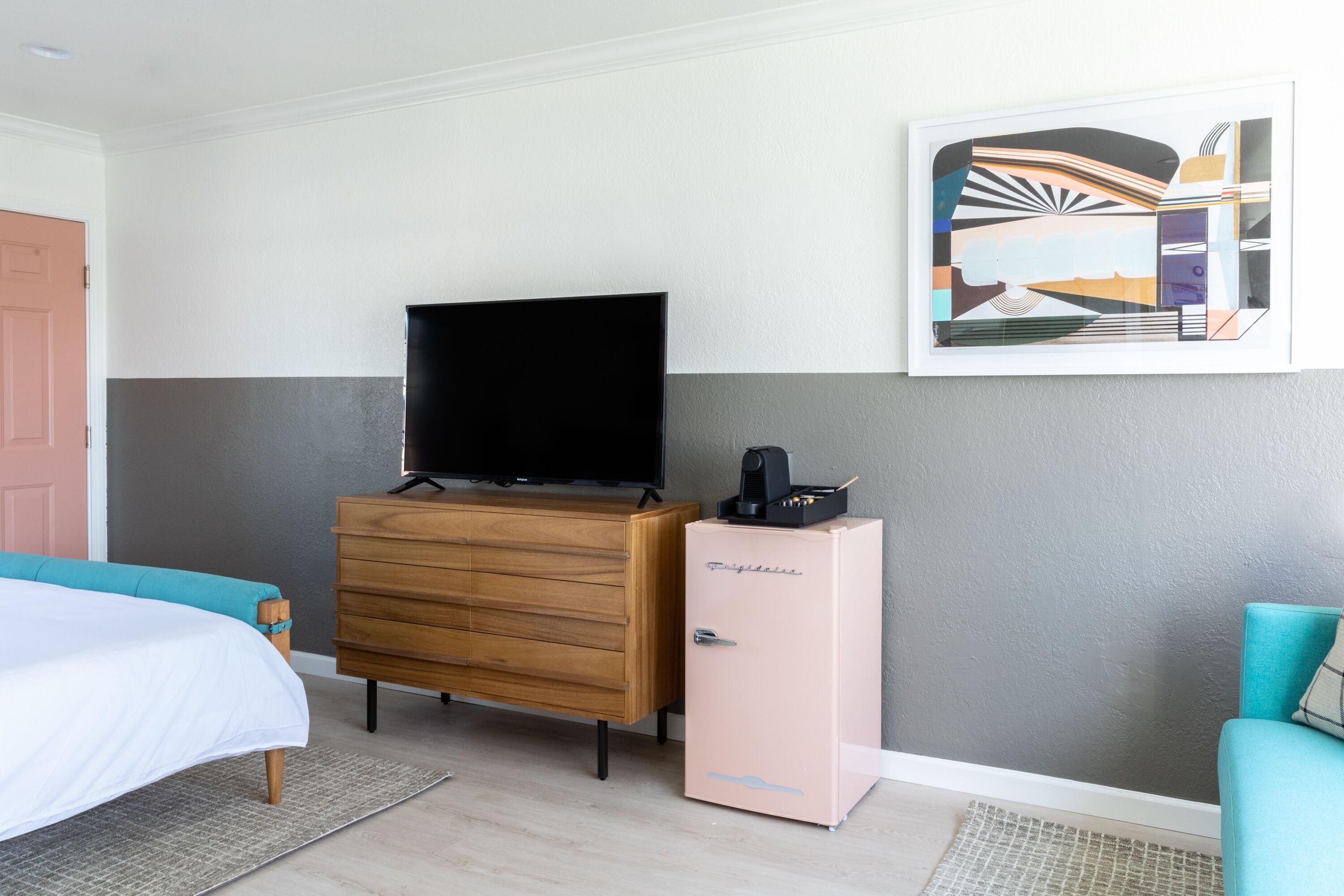 Une chambre d’hôtel avec un lit, une commode, une télévision, un réfrigérateur et un tableau au mur.