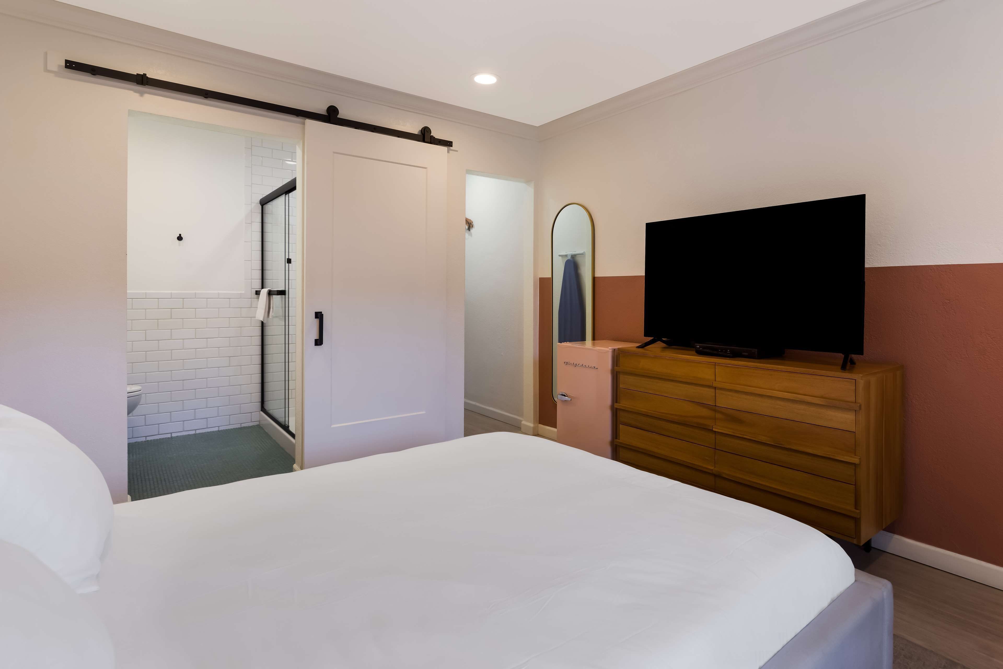A bedroom with a bed, a dresser, a television, and a bathroom with a shower and toilet.