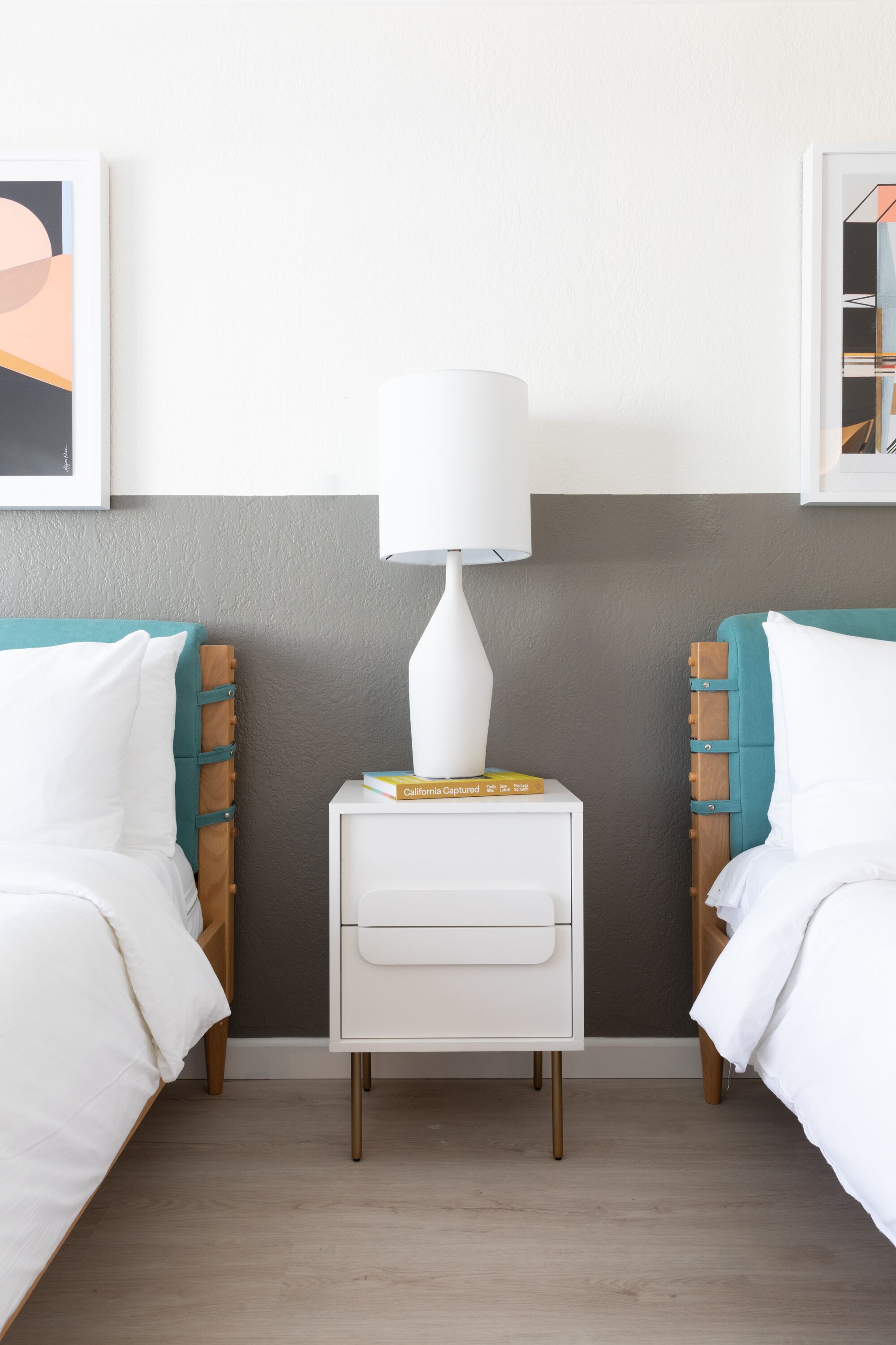 A hotel room with two beds, a nightstand, and a lamp.