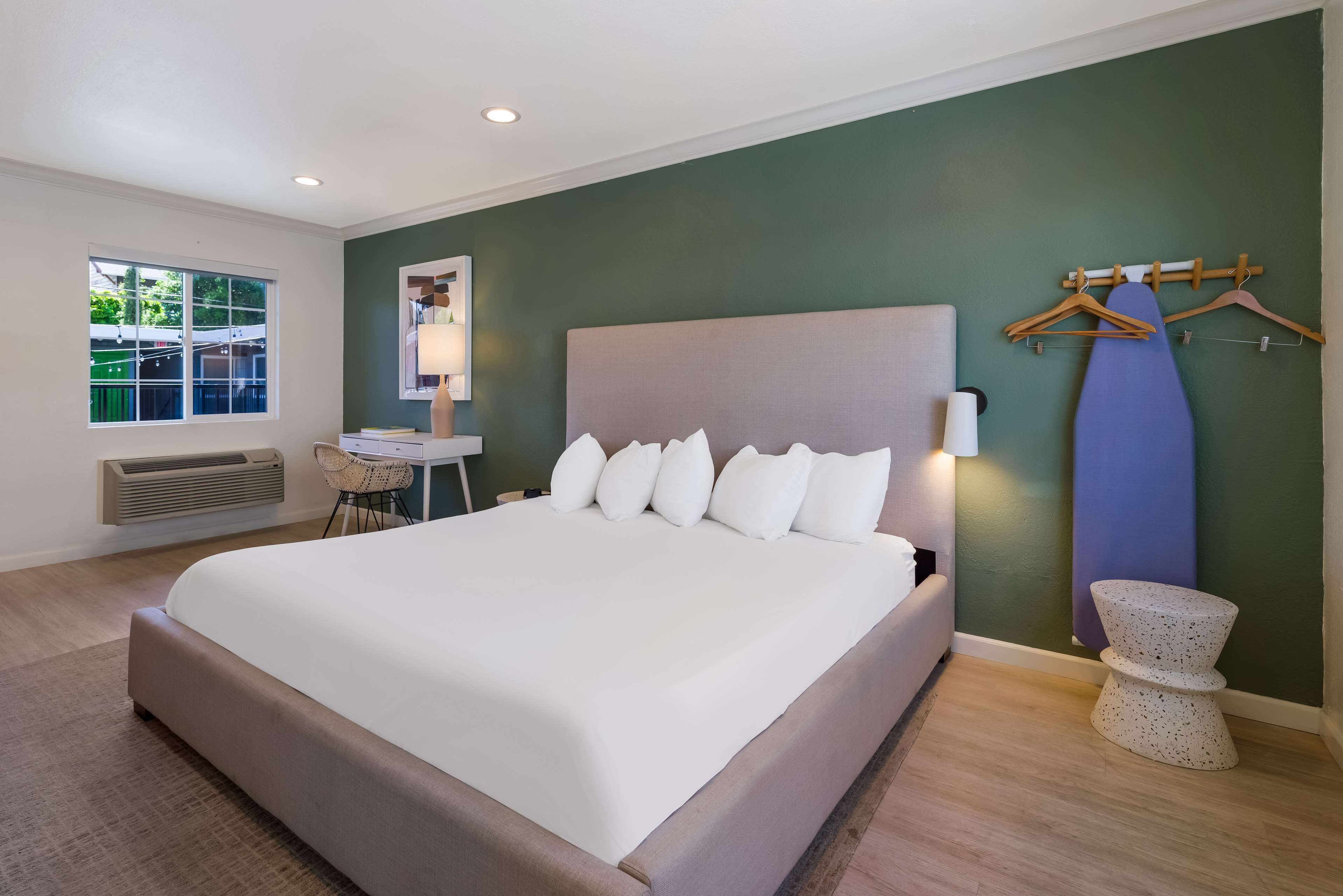 Een verzorgde hotelkamer met een groot bed, een klein bureau, een stoel en een surfboard aan de muur.