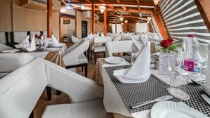 A restaurant with white leather chairs and tables, wooden beams, and hanging light fixtures. - Rose Petal (Srinagar)