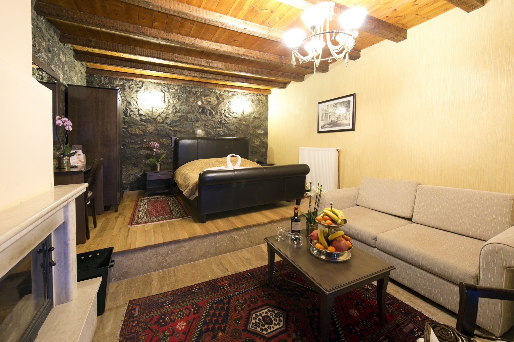 A cozy living room with a stone wall, a fireplace, a sofa, a coffee table with fruit, and a bed with a headboard.