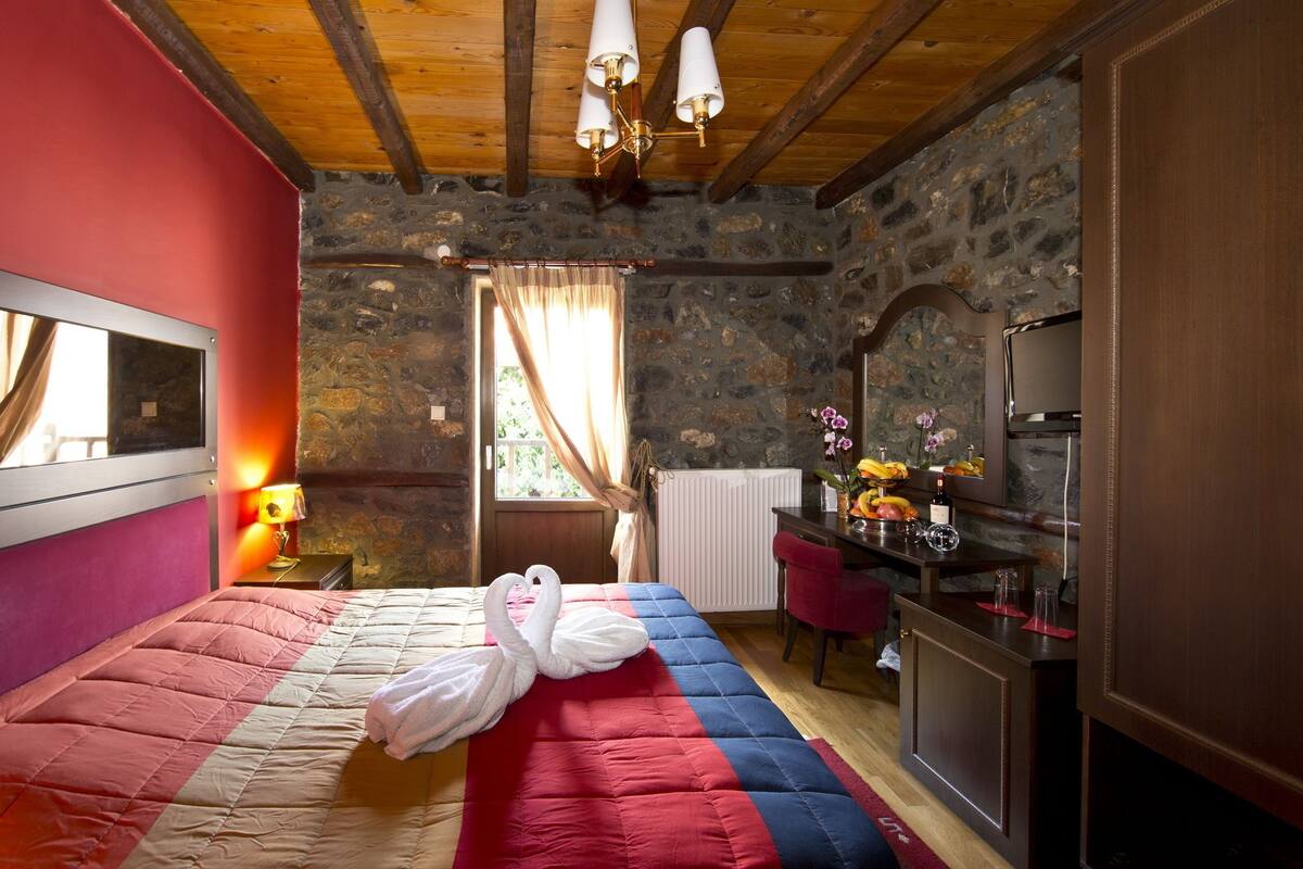 A bedroom with a bed, a dresser, a vanity, and a stone wall.