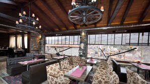 Un restaurante con pared de piedra, grandes ventanales y vista a la ciudad.