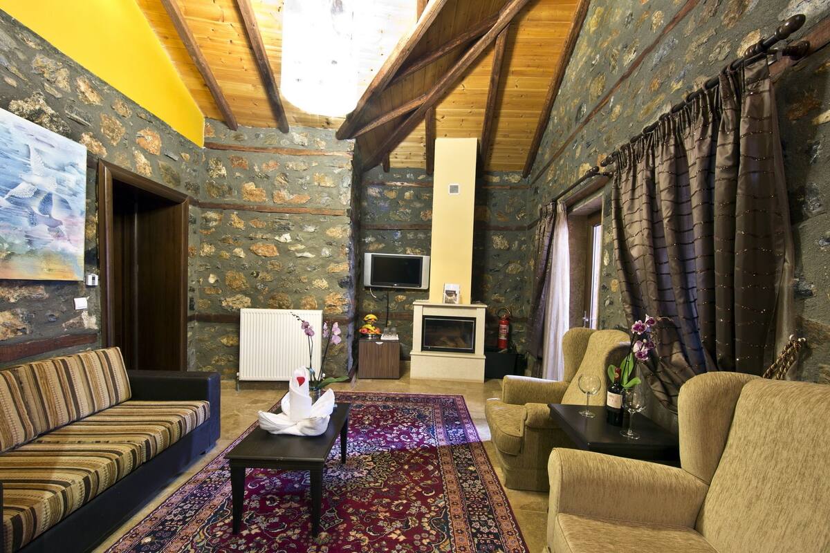 A cozy living room with a stone wall, a fireplace, a television, and a sofa.