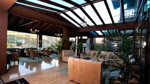 Un vestíbulo espacioso con techo alto, ventanas amplias y un área de descanso con sofás y sillones.