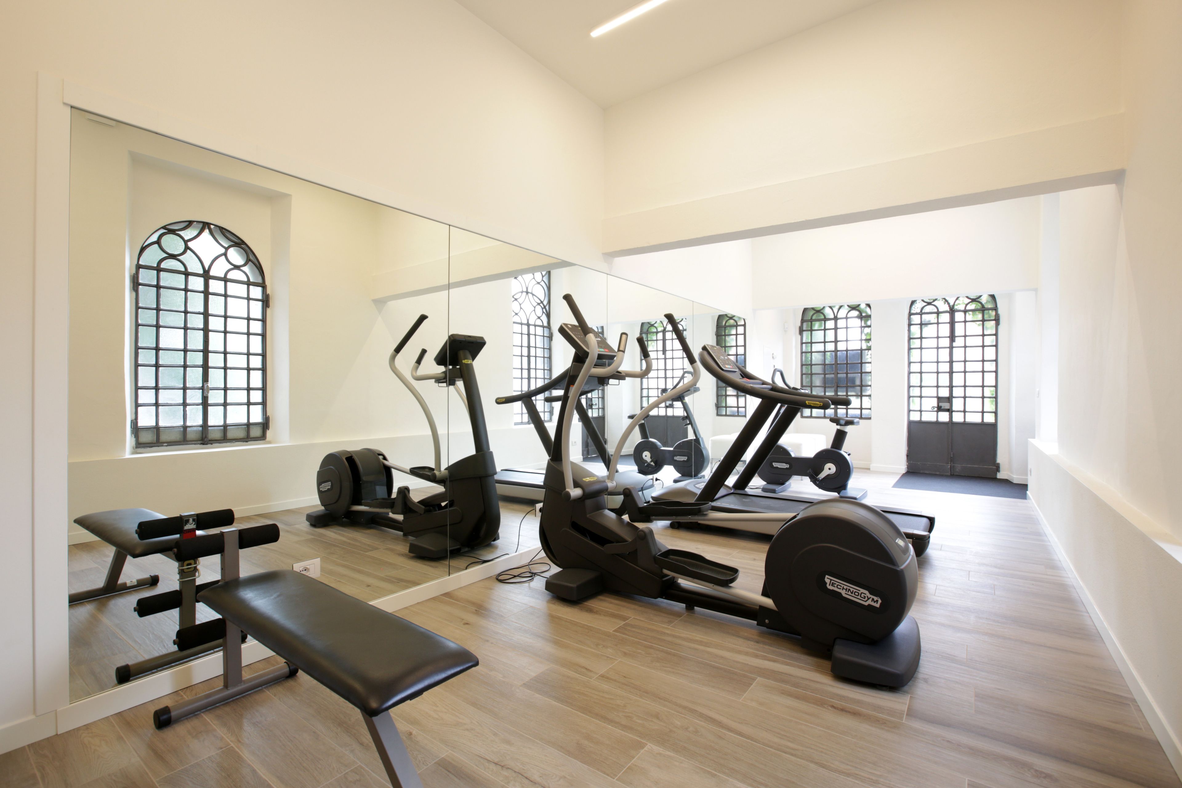 Un gimnasio con equipo de ejercicio, una banca y ventanas amplias.
