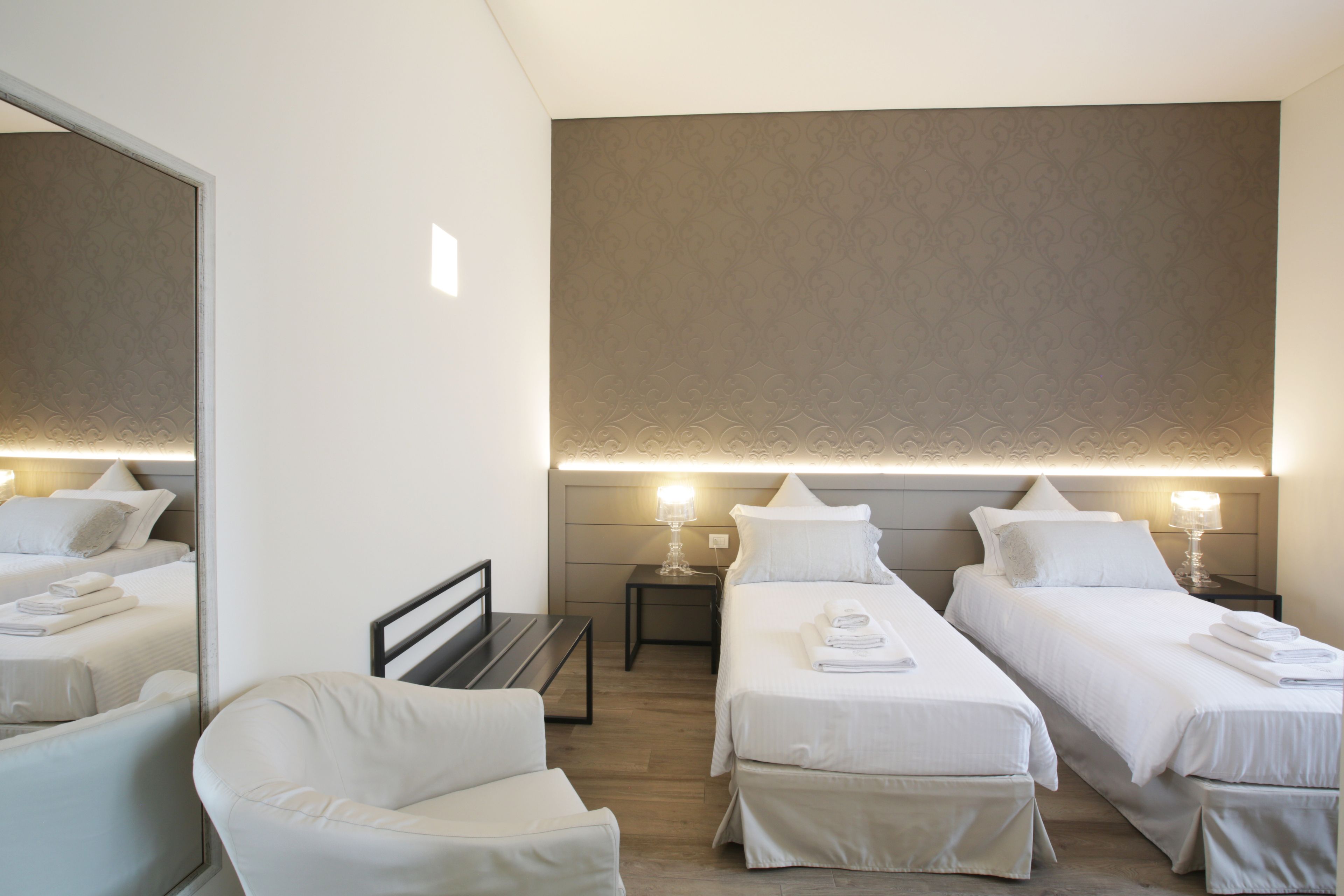 A hotel room with two single beds, a bench, a chair, and a large mirror.