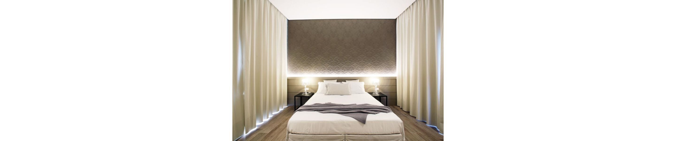 Una habitación de hotel moderna con una cama grande, lámparas de noche y un cabecero estampado.