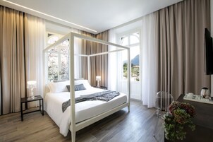 Una habitación de hotel moderna con una cama con dosel, una mesita de noche pequeña con una lámpara, un escritorio con una silla y un ventanal que ofrece vistas al exterior.