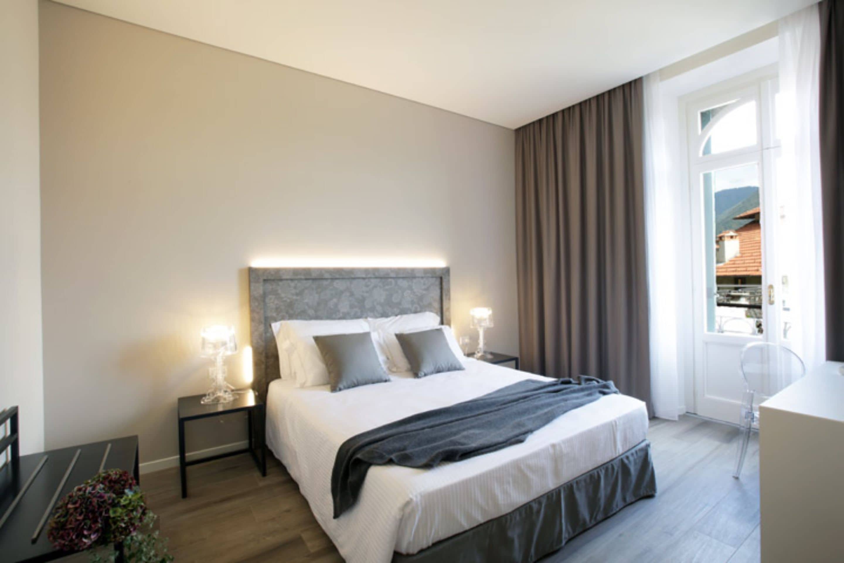 Habitación de hotel moderna con una cama grande, lámparas de noche, un escritorio y vistas al exterior.