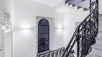 Una escalera con barandilla de hierro forjado negro y pared blanca con un ventanal decorativo.