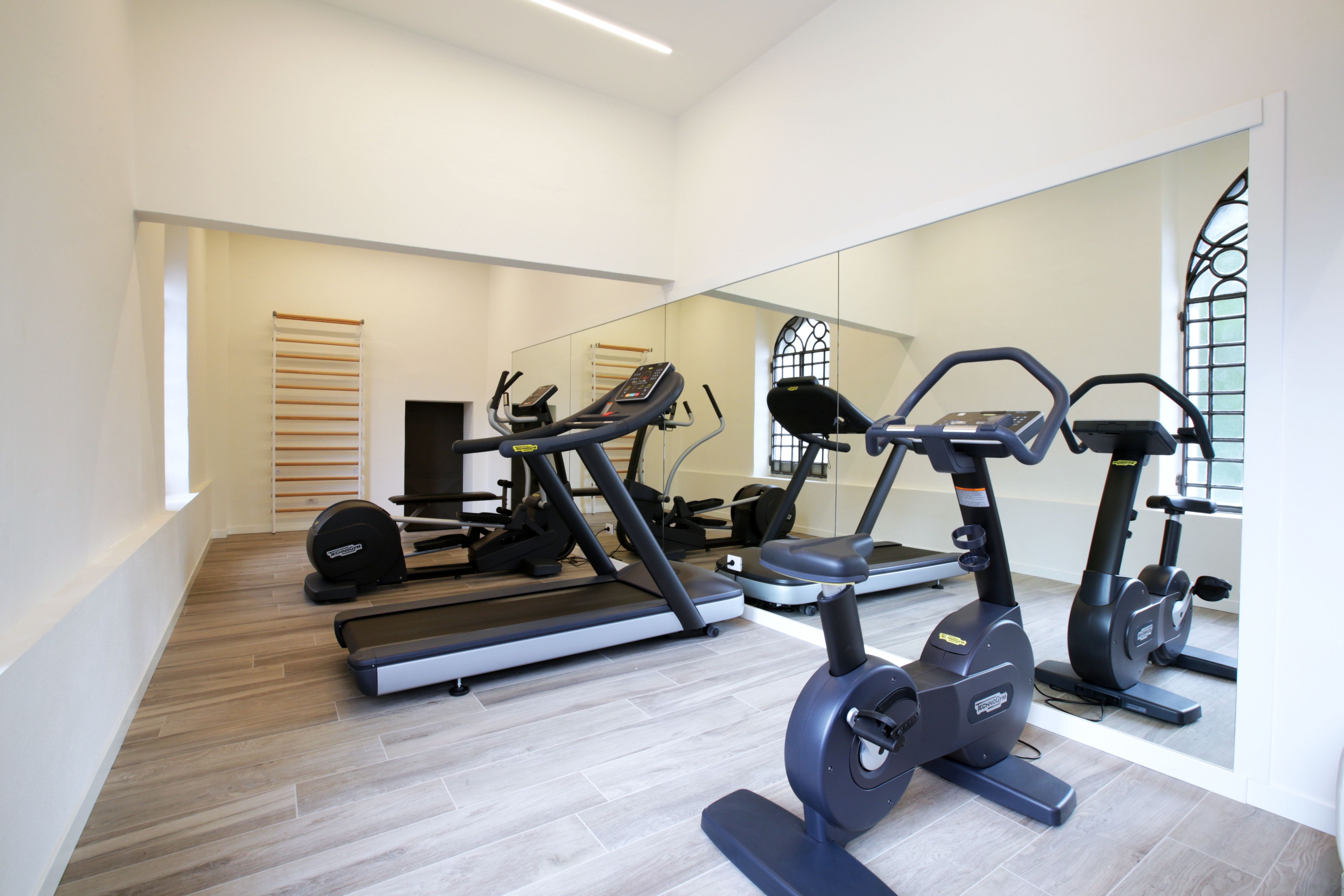 A gym with exercise equipment, a large mirror, and a wooden floor.