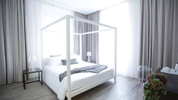A modern bedroom with a four-poster bed, a bedside table with a lamp, and a desk with a vase of flowers.