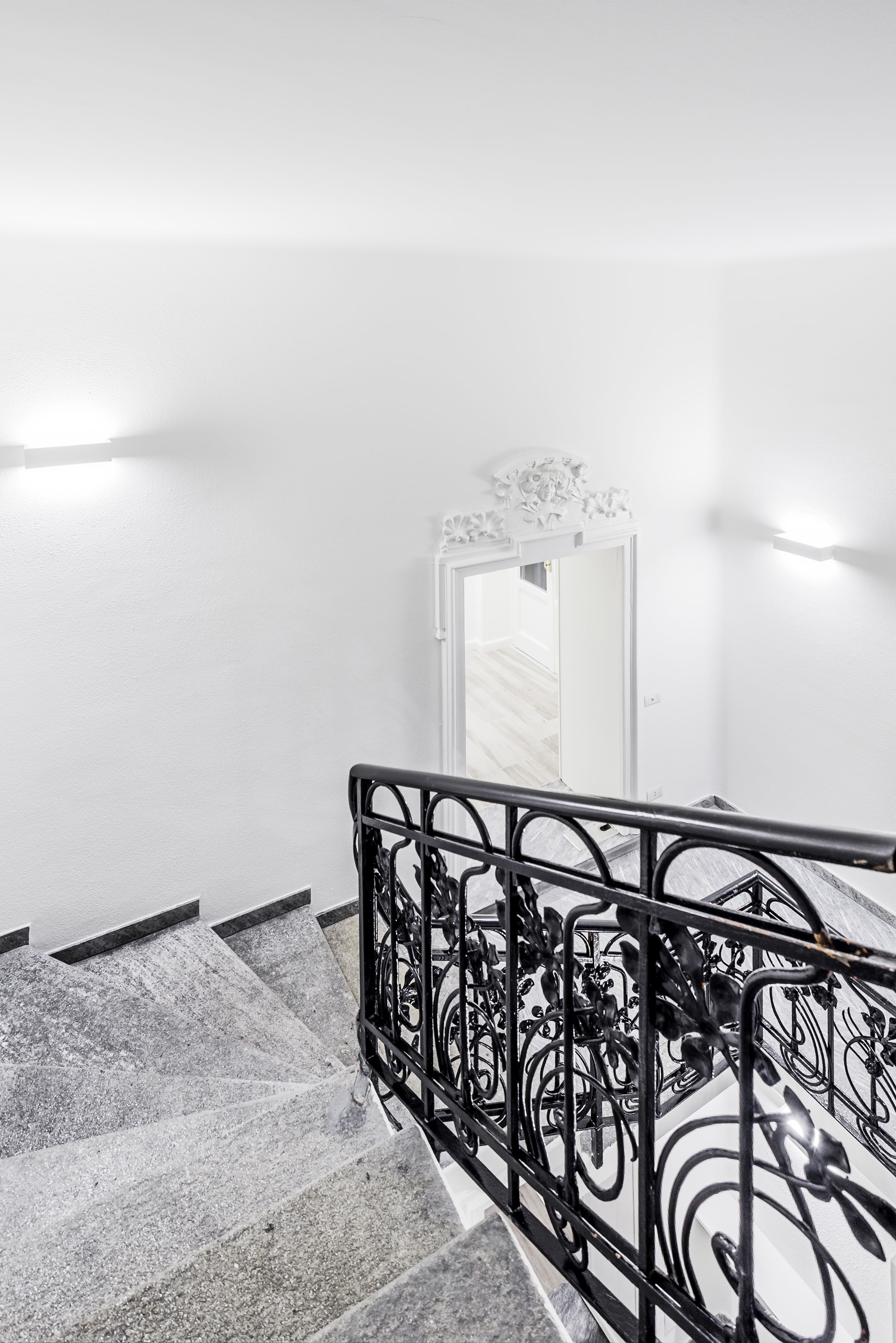 A staircase with a black metal railing and a white wall.