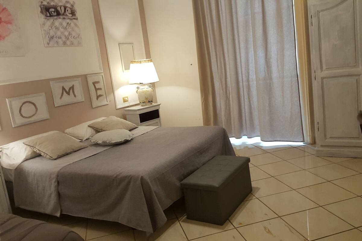 A bedroom with a bed, pillows, a nightstand, a lamp, and a mirror.