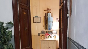 A hallway with a wooden door on the left, a white cabinet with a mirror above it, and a potted plant on the left side. - B&B Napoli Centro (Naples)