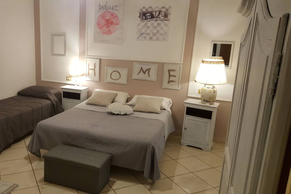 A bedroom with two beds, a bedside table with a lamp, a small table with a basket, and a chair.