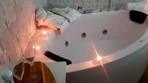 A modern bathroom with a large bathtub, a glass of wine, and a bottle of Santero on the counter. - B&B Napoli Centro (Naples)