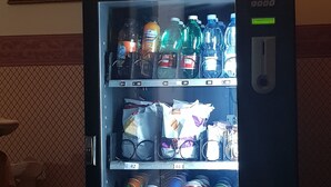 A vending machine with various drinks and snacks, a framed painting of a historical building, and a tiled wall with a geometric pattern. - B&B Napoli Centro (Naples)