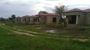 A row of unfinished brick buildings with red-tiled roofs, a dirt path, and sparse vegetation. - Hlakula Lake Resort (Metz)