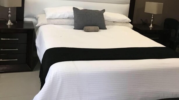 A neatly made bed with a large headboard, two bedside tables with lamps, and a dark-colored nightstand. - Hlakula Lake Resort (Metz)