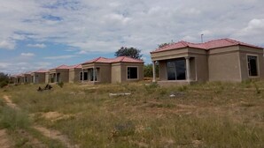 A row of single-story buildings with red-tiled roofs, likely residential units, in a grassy area with a clear sky. - Hlakula Lake Resort (Metz)