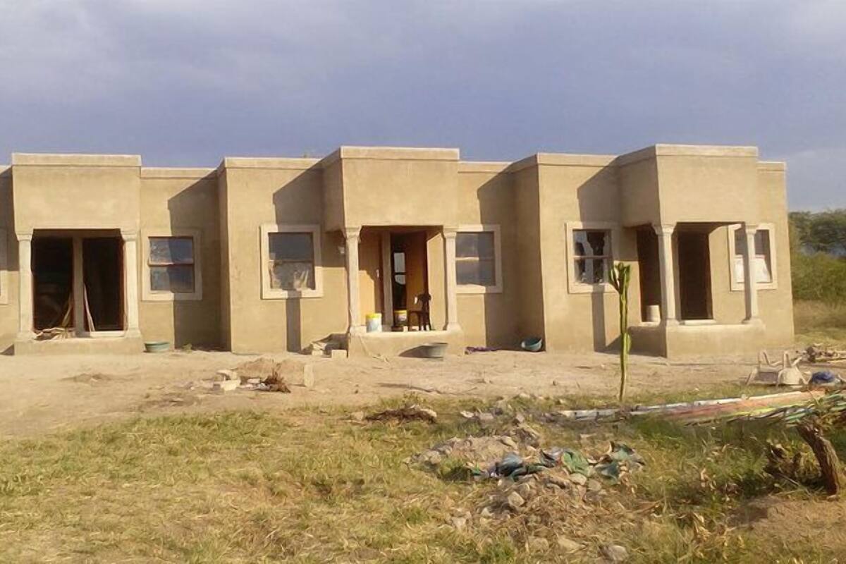 A row of three single-story buildings with flat roofs, each featuring a small porch and a window. The buildings are situated in a dry, grassy area with some debris scattered around.