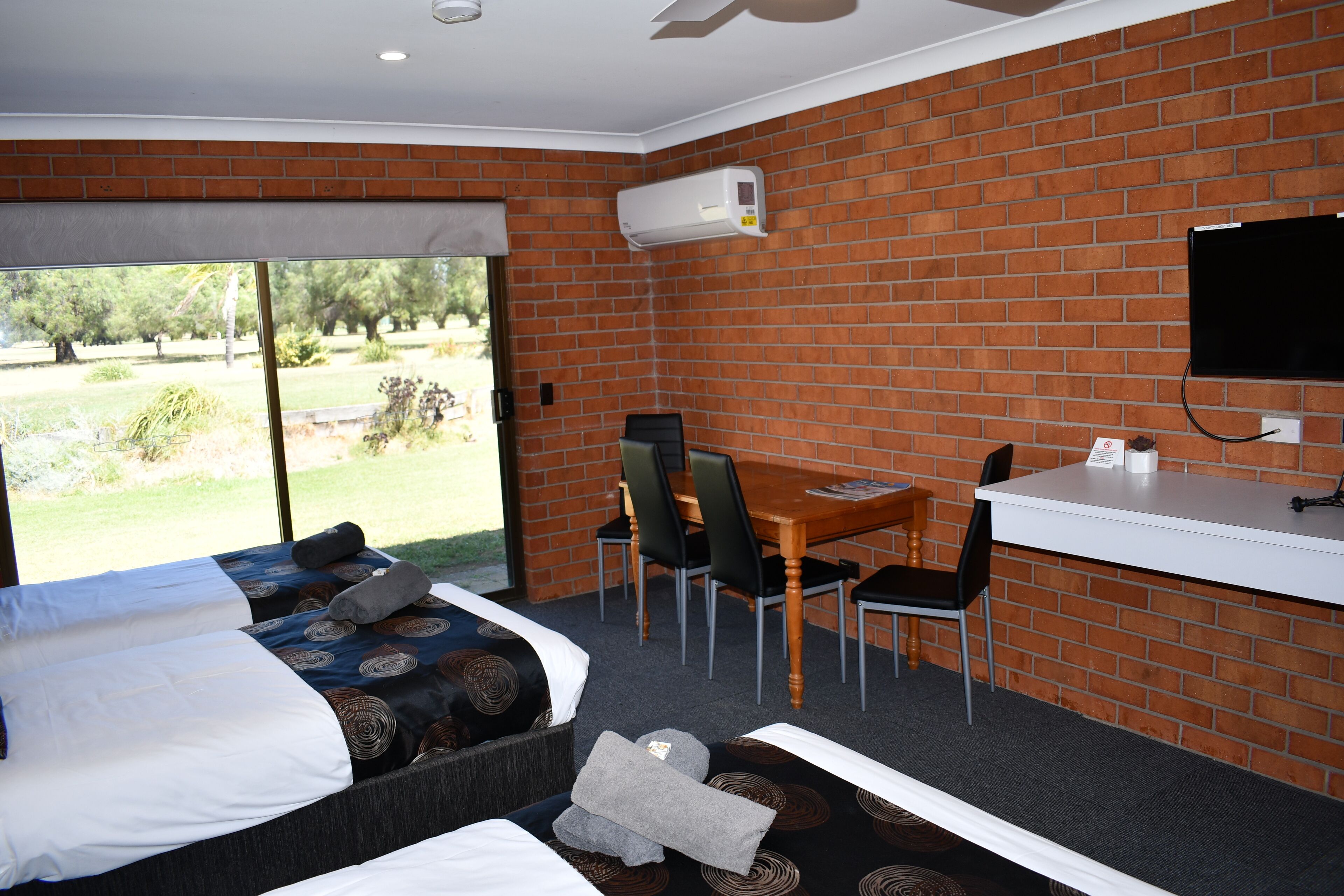 Habitación de hotel con cama, escritorio, silla, televisor y pared de ladrillo.