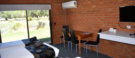 Habitación de hotel con cama, escritorio, silla, televisor y pared de ladrillo.