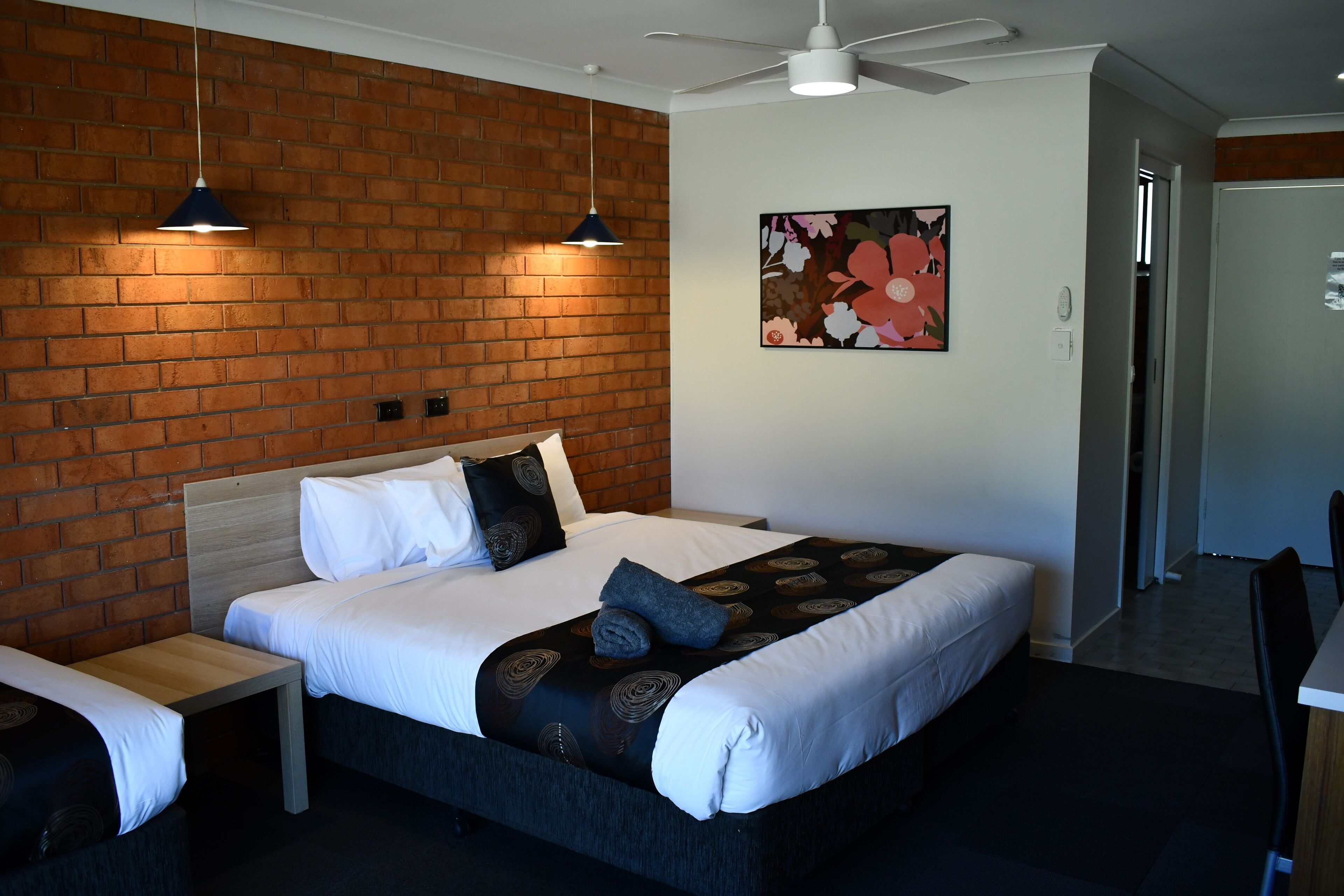 A hotel room with a brick wall, a bed with white bedding, a small table, and a ceiling fan.