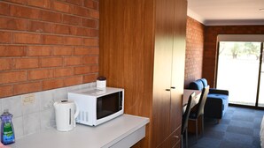 A kitchen with a microwave, kettle, and dish soap on the counter. There is a brick wall and a wooden cabinet. - Berrigan Motel (Berrigan)